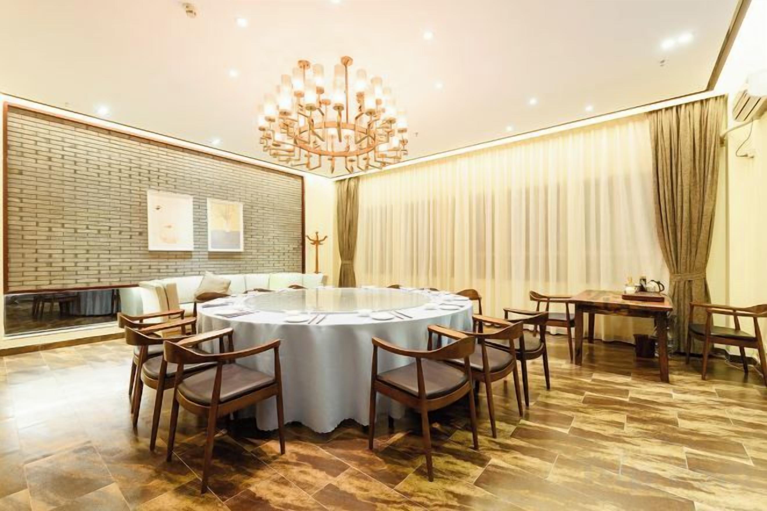 A conference room with a round table, chairs, a chandelier, a brick wall, and a window with curtains.