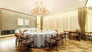 A conference room with a round table, chairs, a chandelier, a brick wall, and a window with curtains.