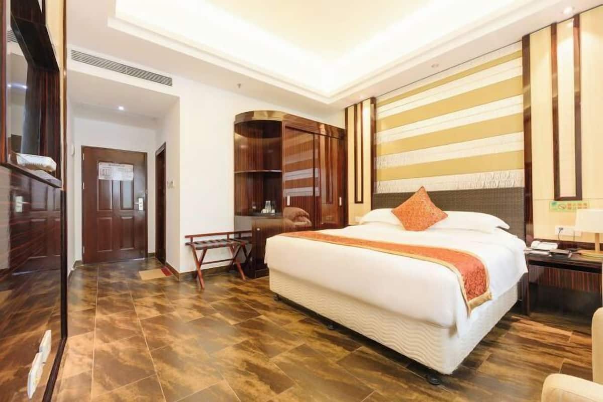 Une chambre d’hôtel avec un grand lit, un bureau, une chaise, une armoire et un miroir.