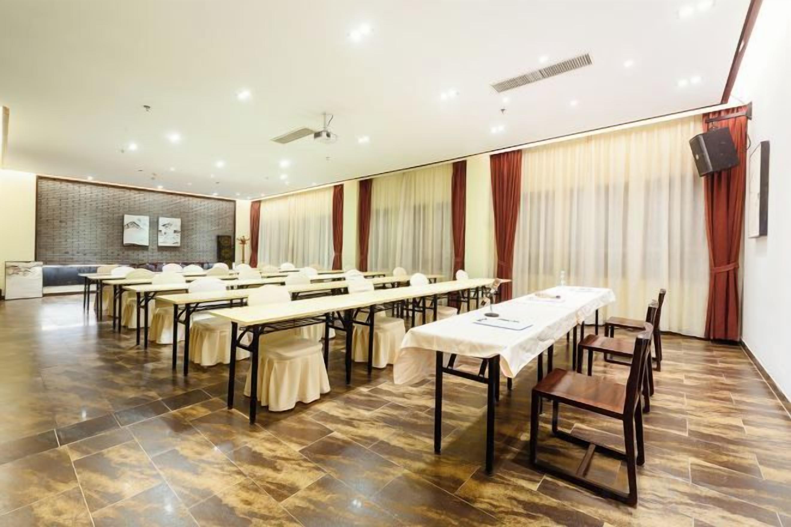 Un salón de conferencias con varias mesas y sillas, una pizarra y una pantalla de proyector.