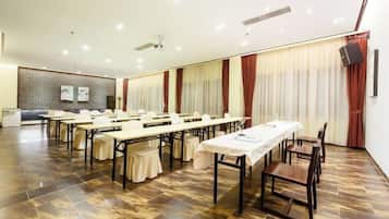 Un salón de conferencias con varias mesas y sillas, una pizarra y una pantalla de proyector.