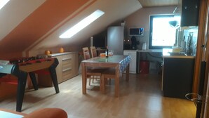 Ein Dachzimmer mit Kicker, Esstisch und einer Küchenzeile mit Mikrowelle.