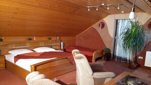 Ein Zimmer mit Holzwänden, einem Bett, einer Couch, einem Sessel, einem Tisch und einer Topfpflanze.