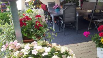 A patio area with a table and chairs, surrounded by potted plants and flowers.