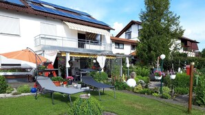 Ein Wohnhausgarten mit einer Terrasse, Gartenmöbeln und verschiedenen Pflanzen.