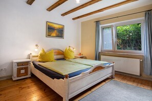 Une chambre à coucher avec un lit en bois, des tables de chevet, un radiateur, une fenêtre avec des rideaux et un tableau accroché au mur.