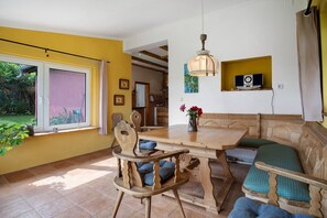 Un espace repas comprenant une table en bois, des chaises, un banc, un luminaire suspendu et une étagère fixée au mur avec un haut-parleur.
