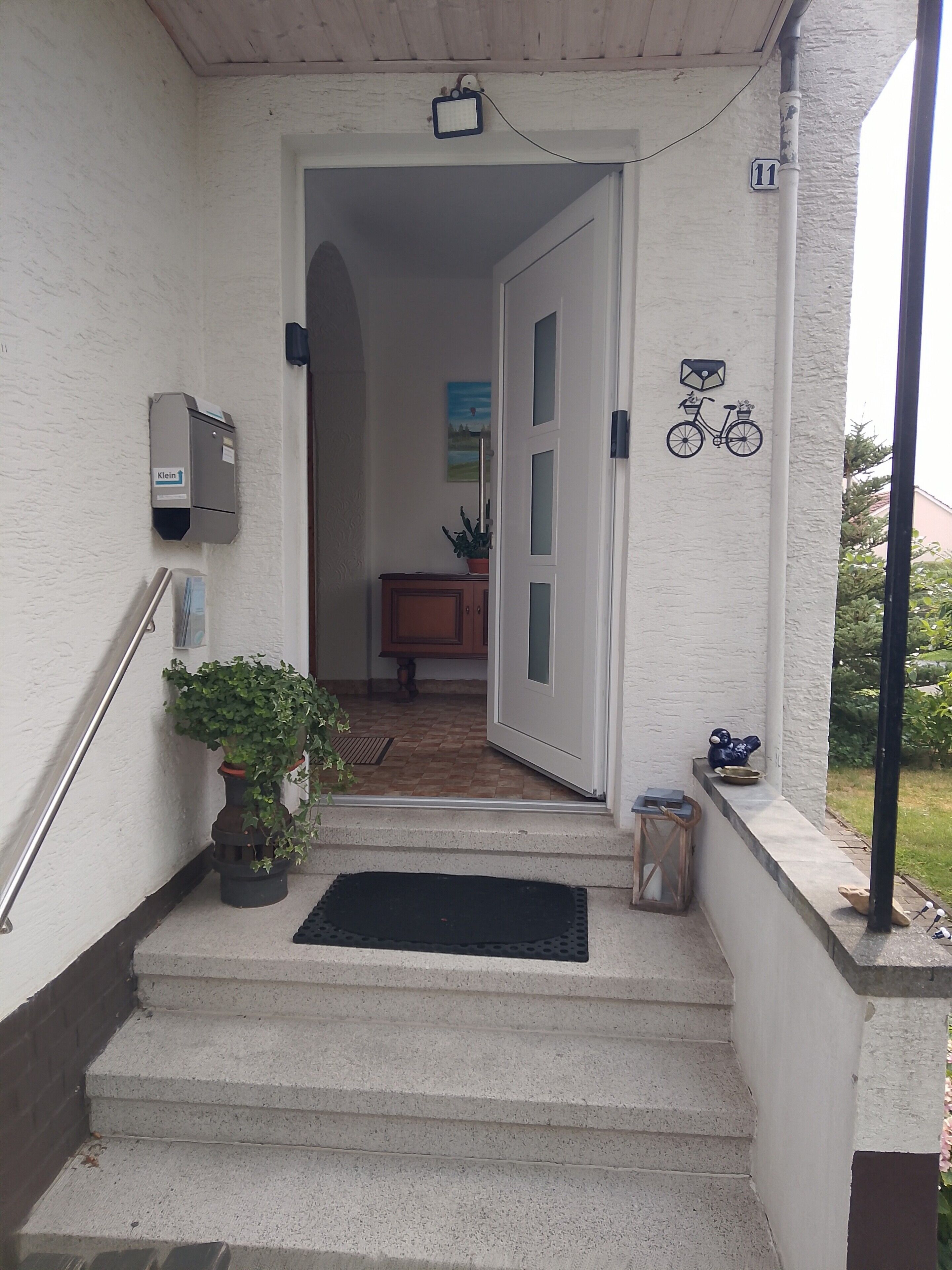 Betonstufen führen zu einer Tür, neben der sich ein Briefkasten und ein Fahrradsymbol an der Wand befinden.