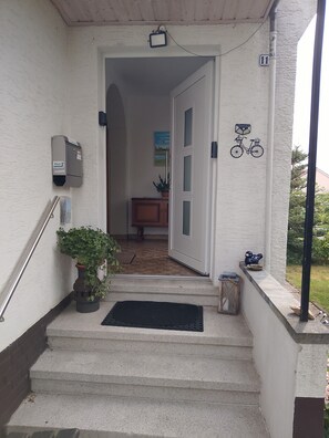 Betonstufen führen zu einer Tür, neben der sich ein Briefkasten und ein Fahrradsymbol an der Wand befinden.