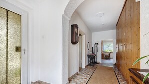 A hallway with a patterned floor, a wooden door, a clock, and a desk with a chair.