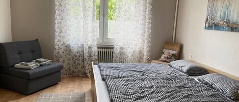 A bedroom with a bed, a sofa, a chair, and a window with curtains.
