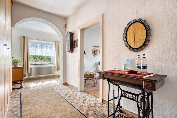 Un pasillo con una máquina de coser antigua, una mesa de madera con botellas y un espejo en la pared.