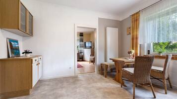 Ein Zimmer mit Holzschrank, Esstisch mit Stühlen, Fernseher im Hintergrund und einem Fenster mit Vorhängen.