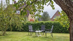 A grassy outdoor area with a table and chairs, a bicycle, and a hedge.