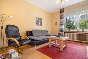 A living room with a leather chair, a sofa, a wooden coffee table, a red rug, a painting, and a view through a window.