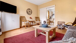 A living room with a TV, a clock, a table with a bowl, and a red rug.