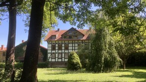 Ein traditionelles Fachwerkhäuschen mit rotem Ziegeldach, umgeben von üppigem Grün und Bäumen.