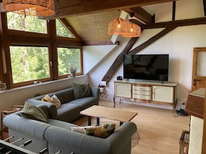 Un salon chaleureux avec un canapé d’angle, un téléviseur et un plafond en bois.