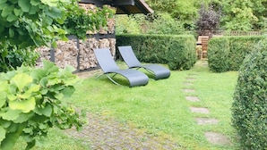 Ein Garten mit einer Holz-Pergola, einer Steinmauer und einer Hecke.