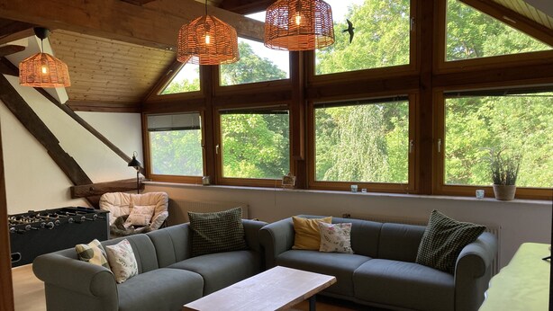 Ein gemütliches Wohnzimmer mit einer Eckcouch, einem Couchtisch und großen Fenstern mit Blick auf Grünflächen.