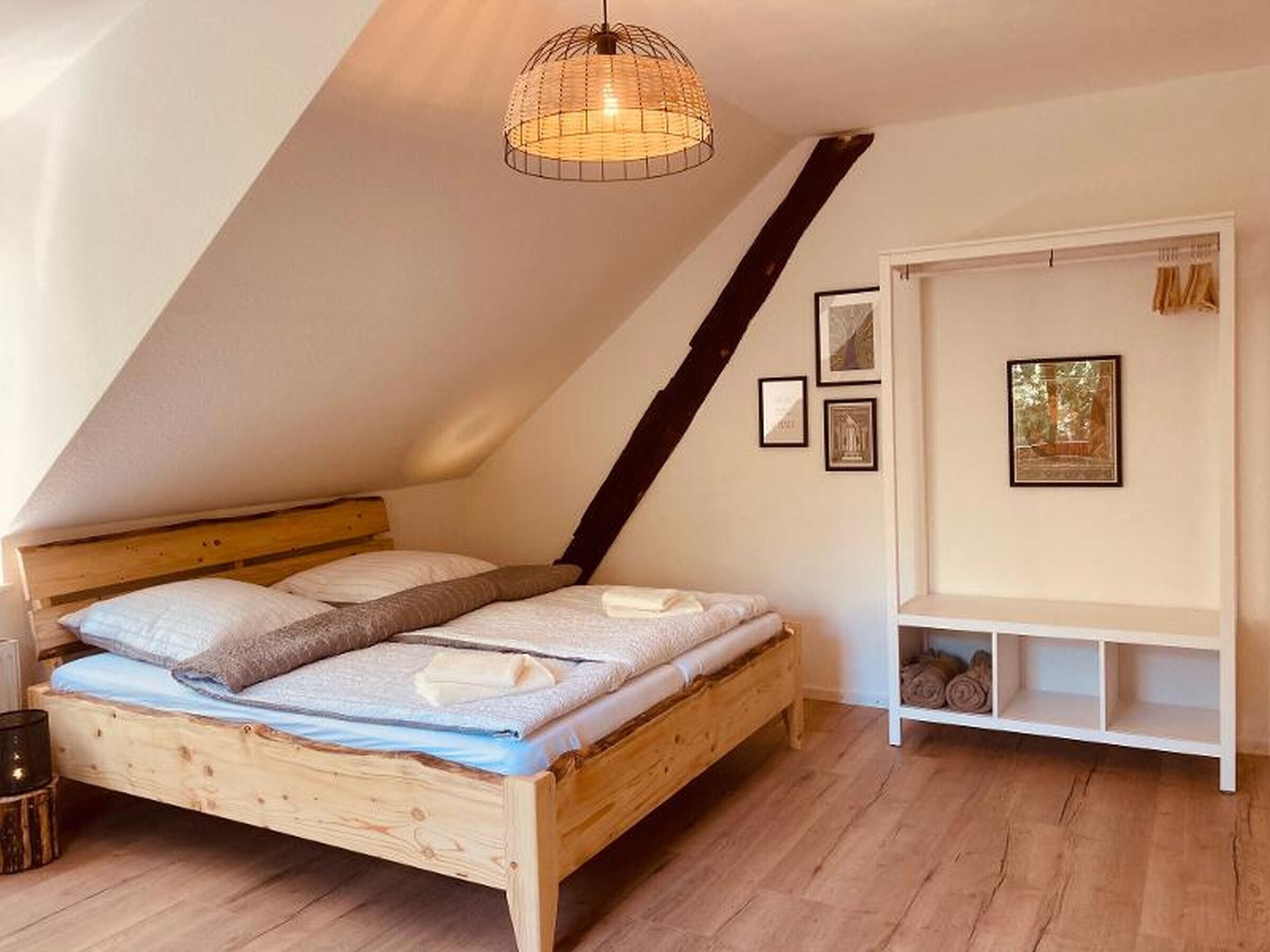 Un dormitorio con techo inclinado, cama de madera, lámpara colgante y estante empotrado blanco con fotografías enmarcadas.