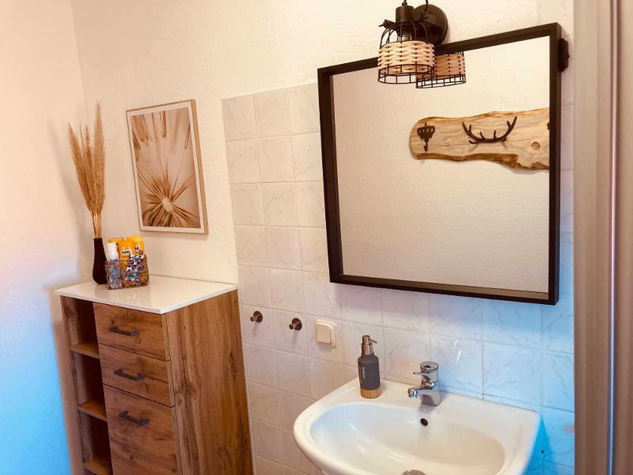 Ein Badezimmer mit einem Holzkosmetikschrank, einem weißen Waschbecken, einem Spiegel und Wanddekoration.