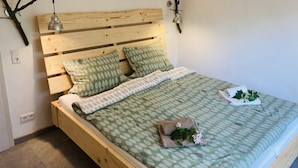 Een houten bed met een sprei met bladpatroon, twee kussens en een kamerplantje op het nachtkastje.