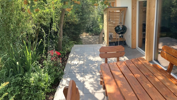 Een houten terras met banken, een barbecue en een schuifdeur die naar een binnenruimte leidt.