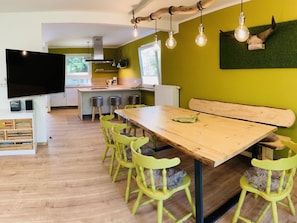 A modern kitchen with a dining area, wooden furniture, and a flat-screen TV.