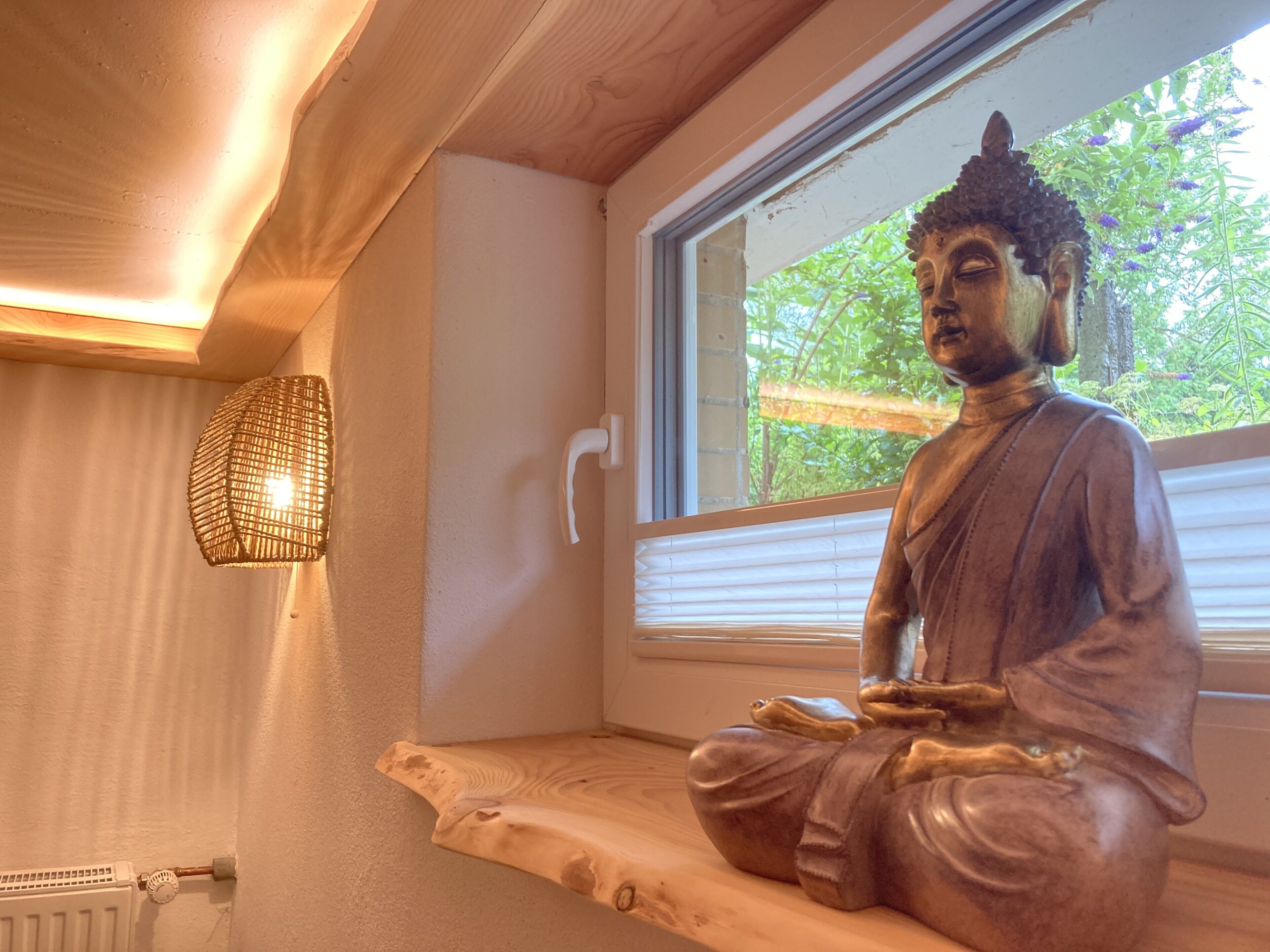 Uma estátua de uma figura sentada em um quarto com janela, radiador e luminária fixada na parede.