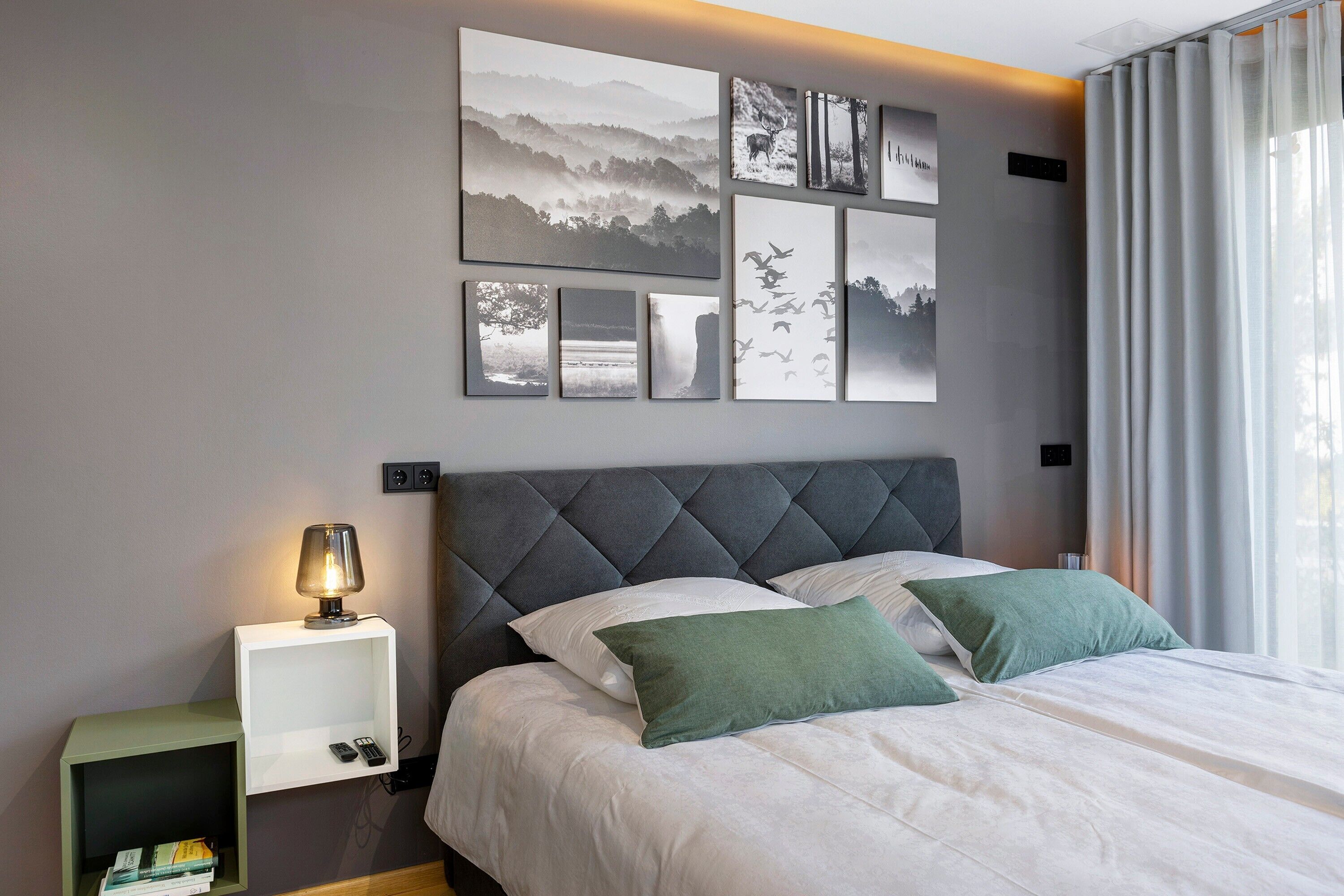 Una camera da letto con un letto, un comodino, una lampada e una parete con quadri.