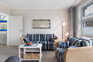 En stue med en sofasæt, et bord med frugt, en lampe og et stort vindue.