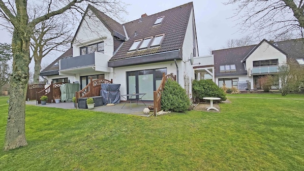Et moderne hus med to etager, en overdækket terrasse, græsplæne og en lille have.