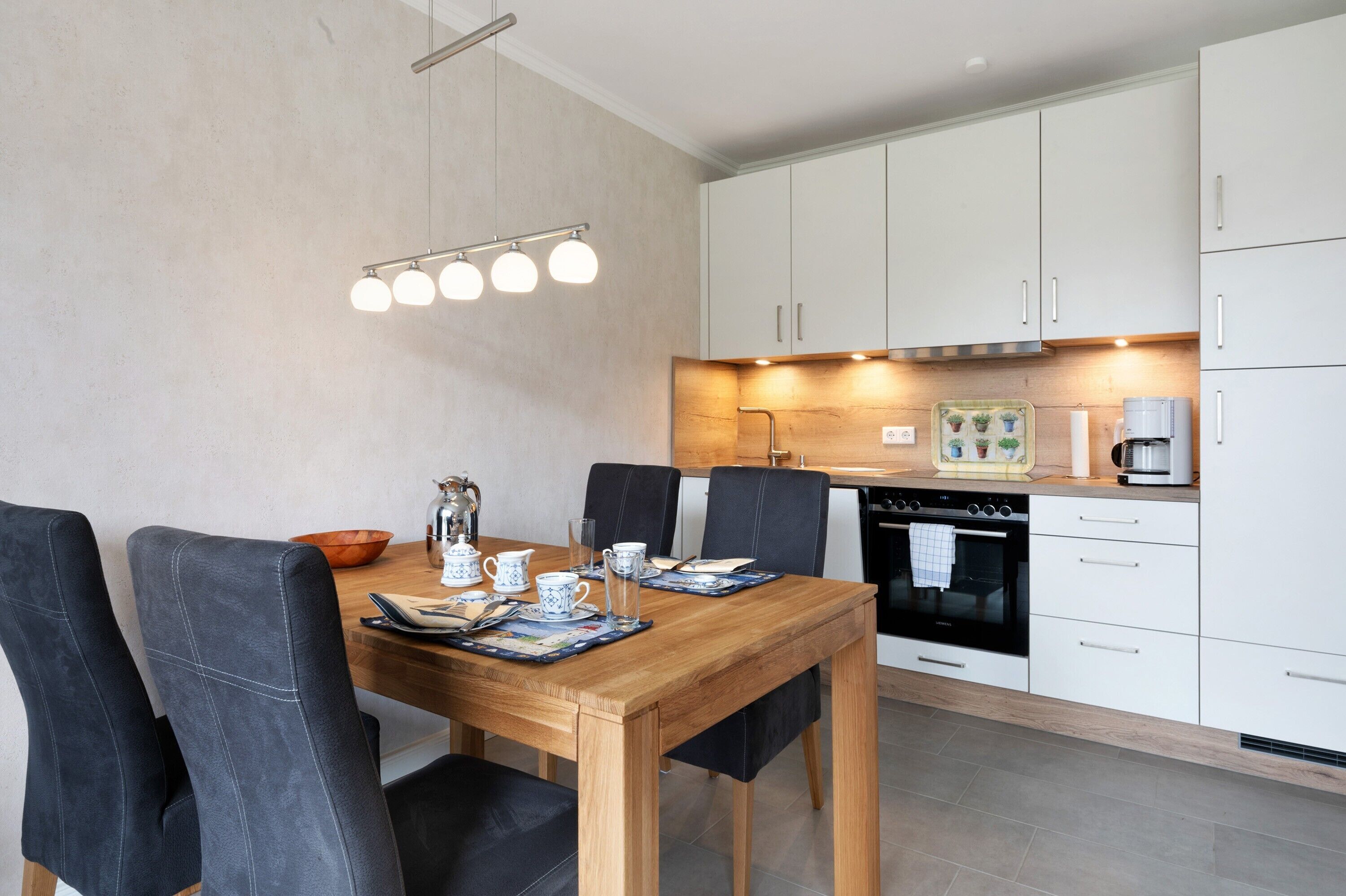 Una cocina moderna con armarios blancos, una mesa de comedor de madera y una cafetera.