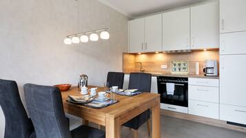 Una cocina moderna con armarios blancos, una mesa de comedor de madera y una cafetera.