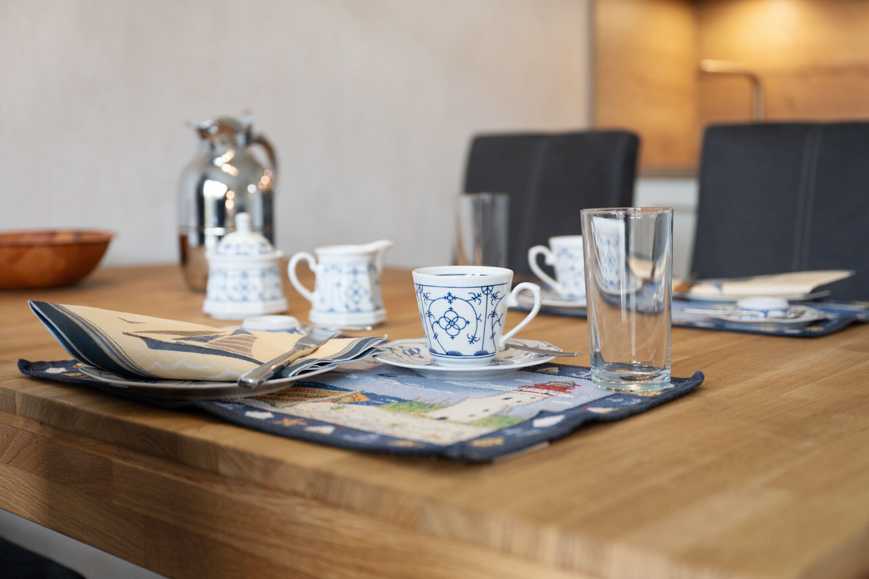 Une table en bois, avec un set de table, une théière, une tasse, un verre et un bol.