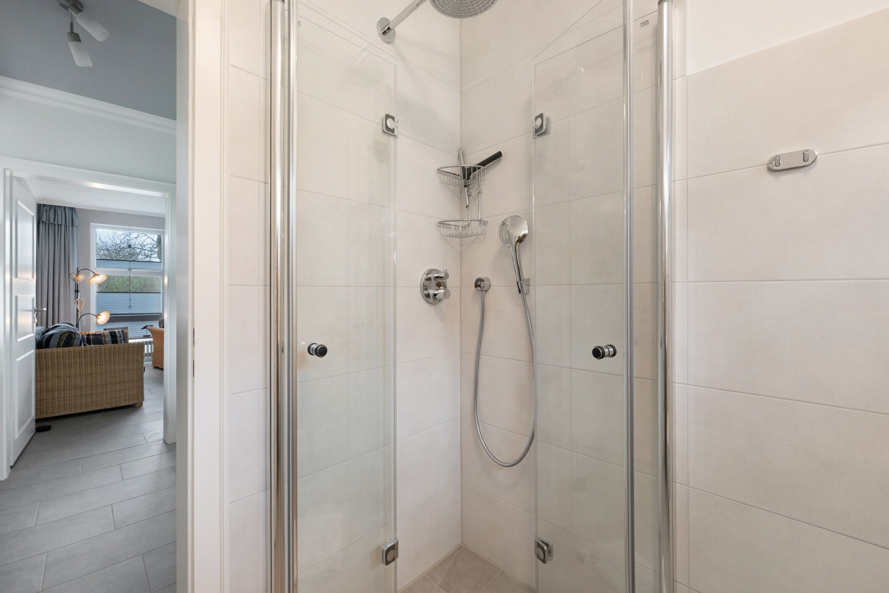 Een douchecabine met glazen wanden, een handdouche en een kraan op de muur.