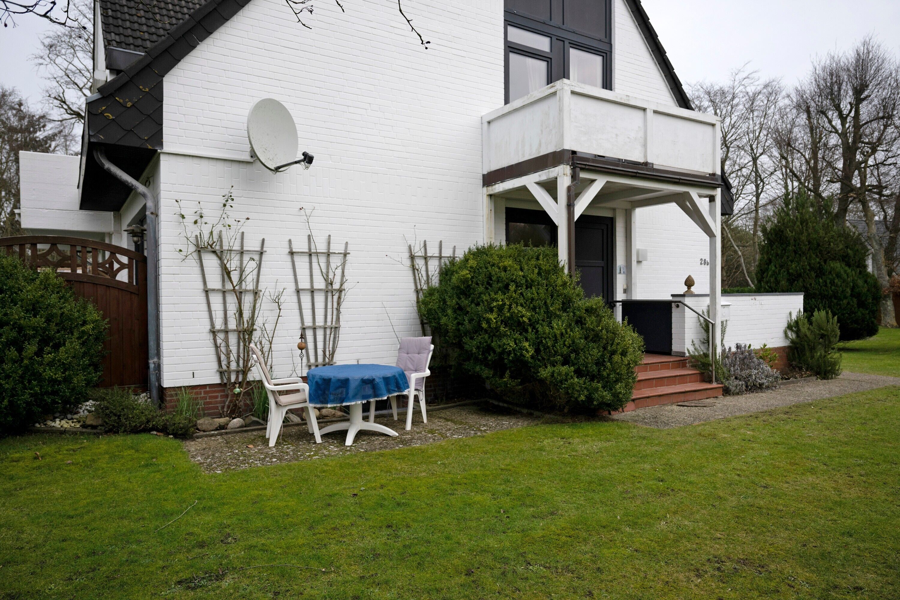 Een wit huis met een schotelantenne, een overdekte veranda en een kleine tafel met stoelen.