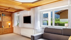 Un salon moderne avec un canapé, un téléviseur, des meubles en bois et une fenêtre donnant sur un paysage verdoyant.