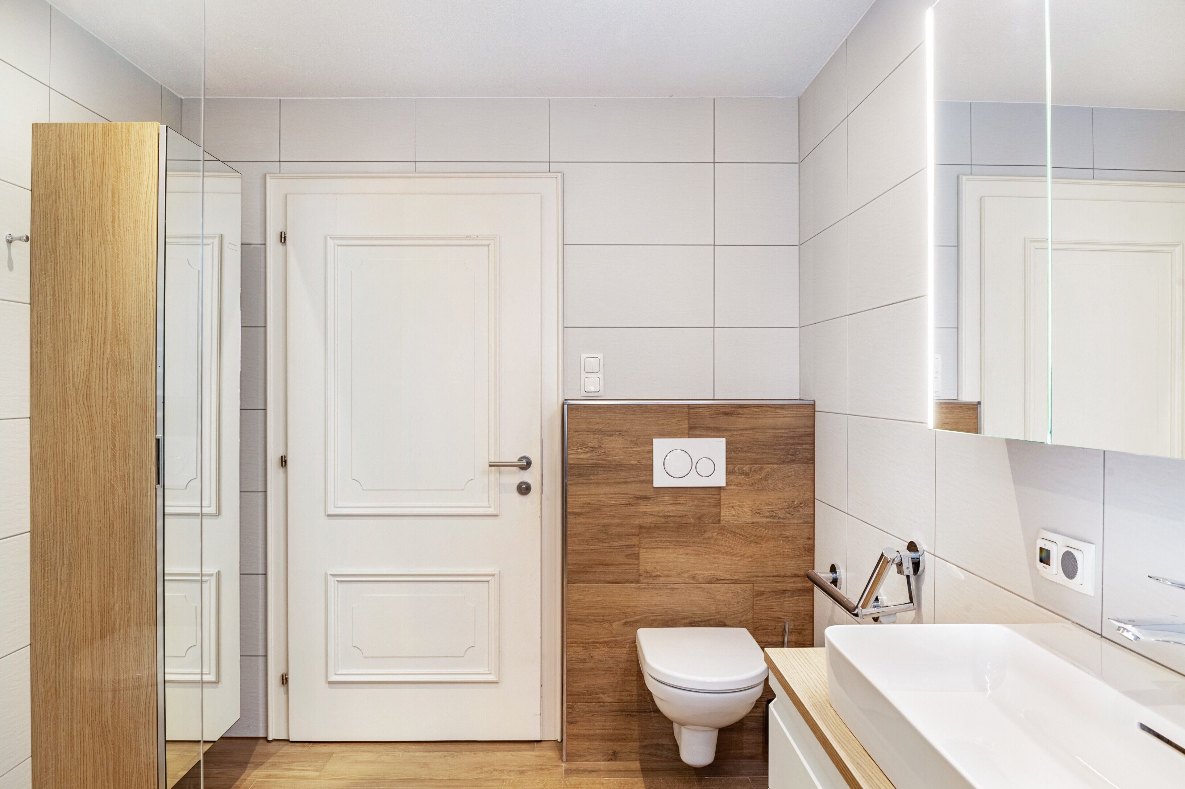 Un baño moderno con tocador de madera, inodoro blanco y espejo grande.