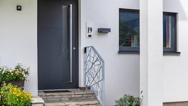 Une entrée moderne avec une porte sombre, des marches en pierre, une rambarde en métal et des plantes en pot.