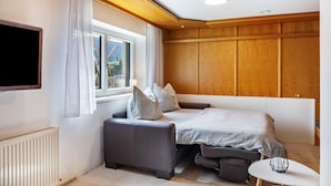 Une chambre à coucher avec un lit, un canapé, une petite table, une télévision et une fenêtre avec des rideaux.
