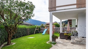 Un jardin avec une balançoire, un toboggan et une terrasse en pierre.