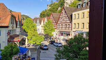 Une place de ville bordée de bâtiments traditionnels à colombages, avec une fontaine et une rue pavée.