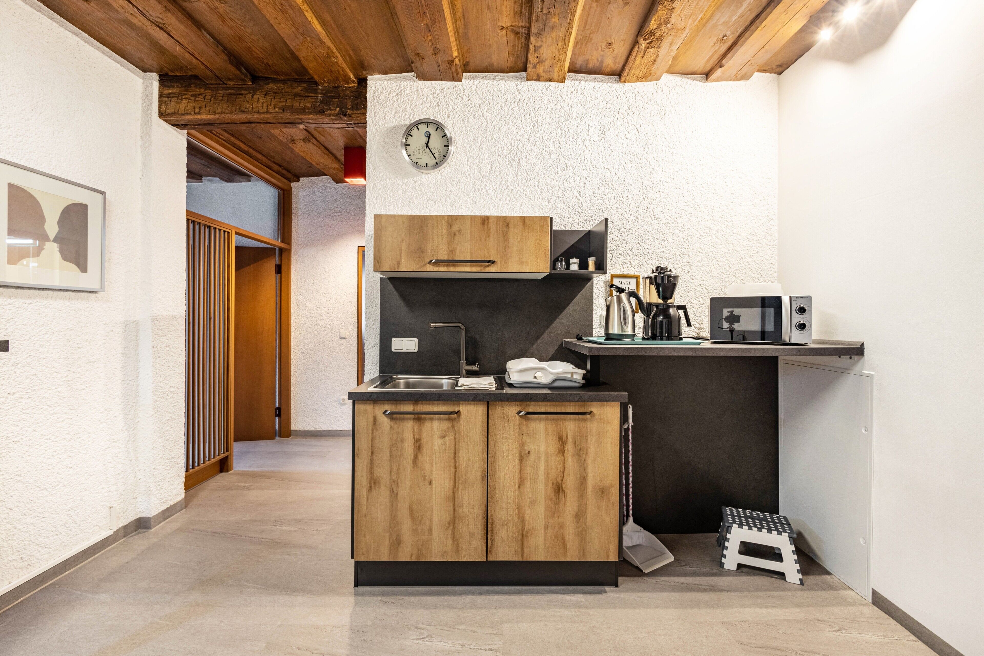 A compact kitchen with wooden cabinets, a coffee machine, and a microwave.