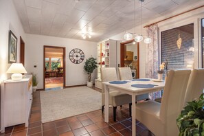 A dining area with a table, chairs, a lamp, a clock, and a potted plant.