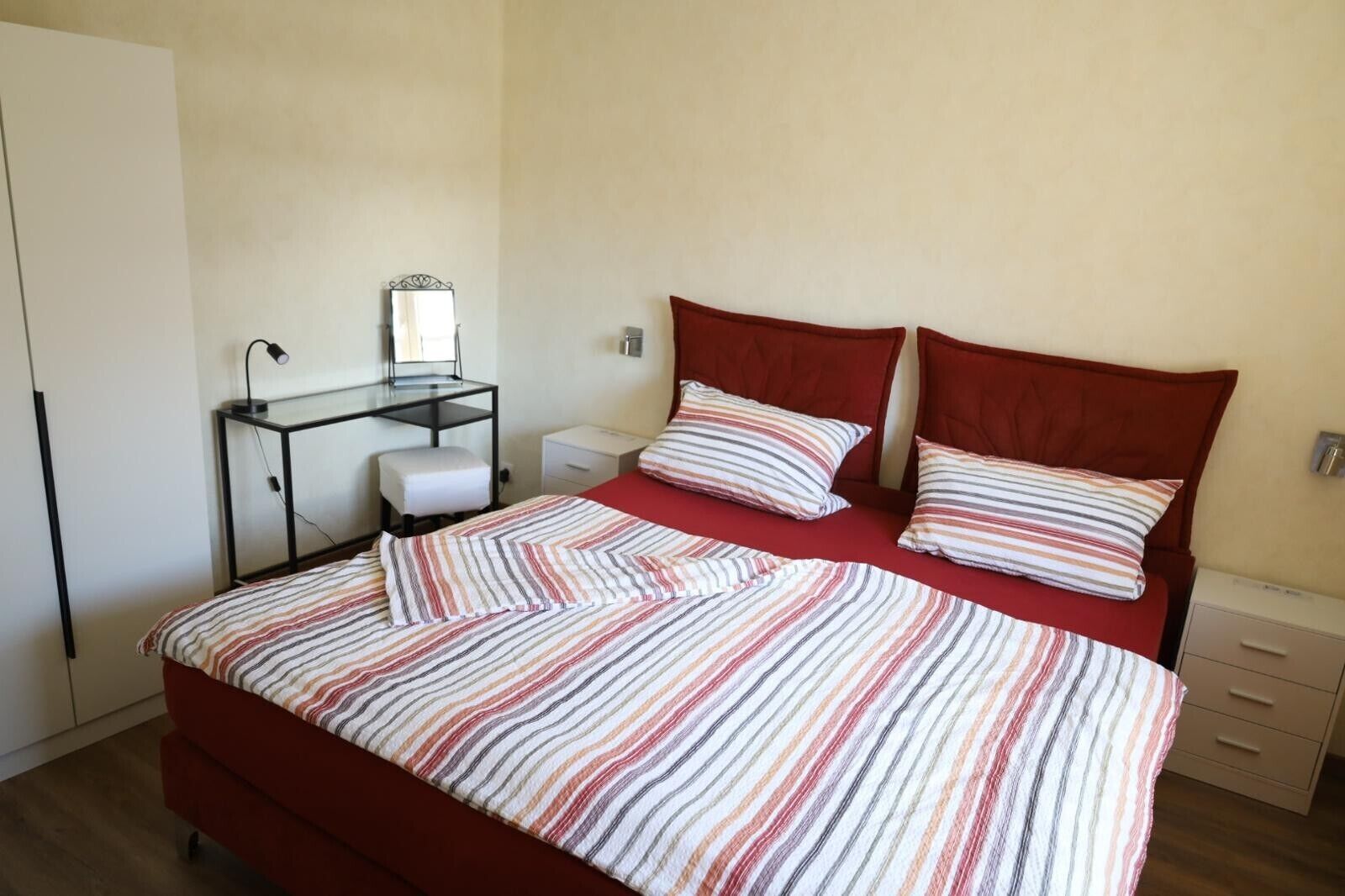 Ein Schlafzimmer mit einem Bett, einem Schreibtisch mit Spiegel, einem Stuhl und einem Nachttisch.