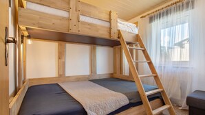 Een stapelbed met een ladder, een nachtkastje en een raam met dunne gordijnen.