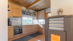 A modern kitchen with wooden cabinets, a built-in oven, and a window overlooking greenery.