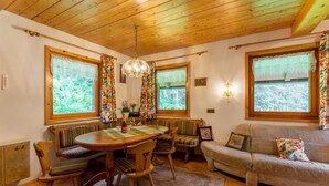 A cozy room with a wooden ceiling, a dining table with chairs, a sofa, and large windows with curtains.